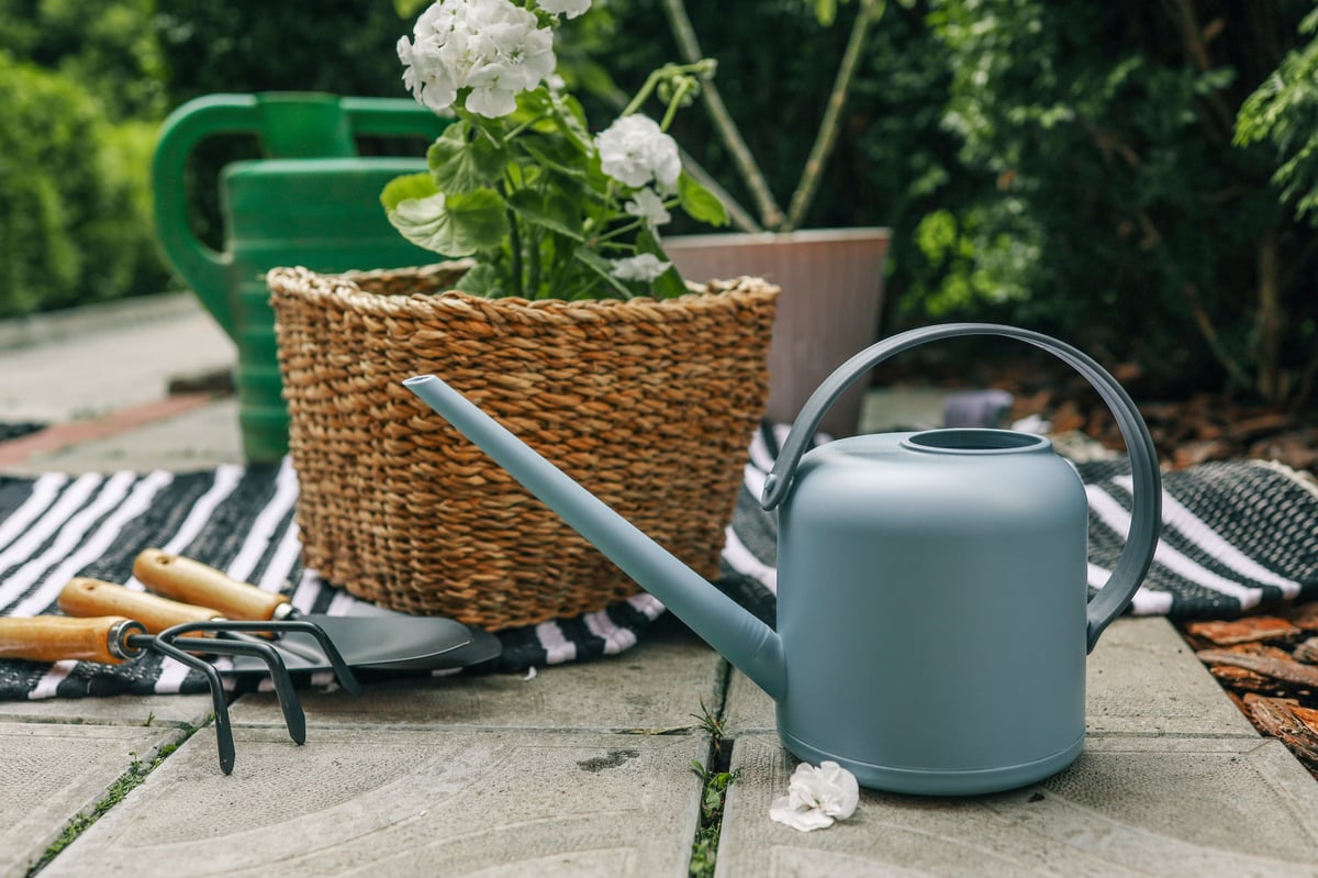 Garden tools and supplies for spring cleanup including basket planter with geraniums, watering can, and garden tools on stone patio