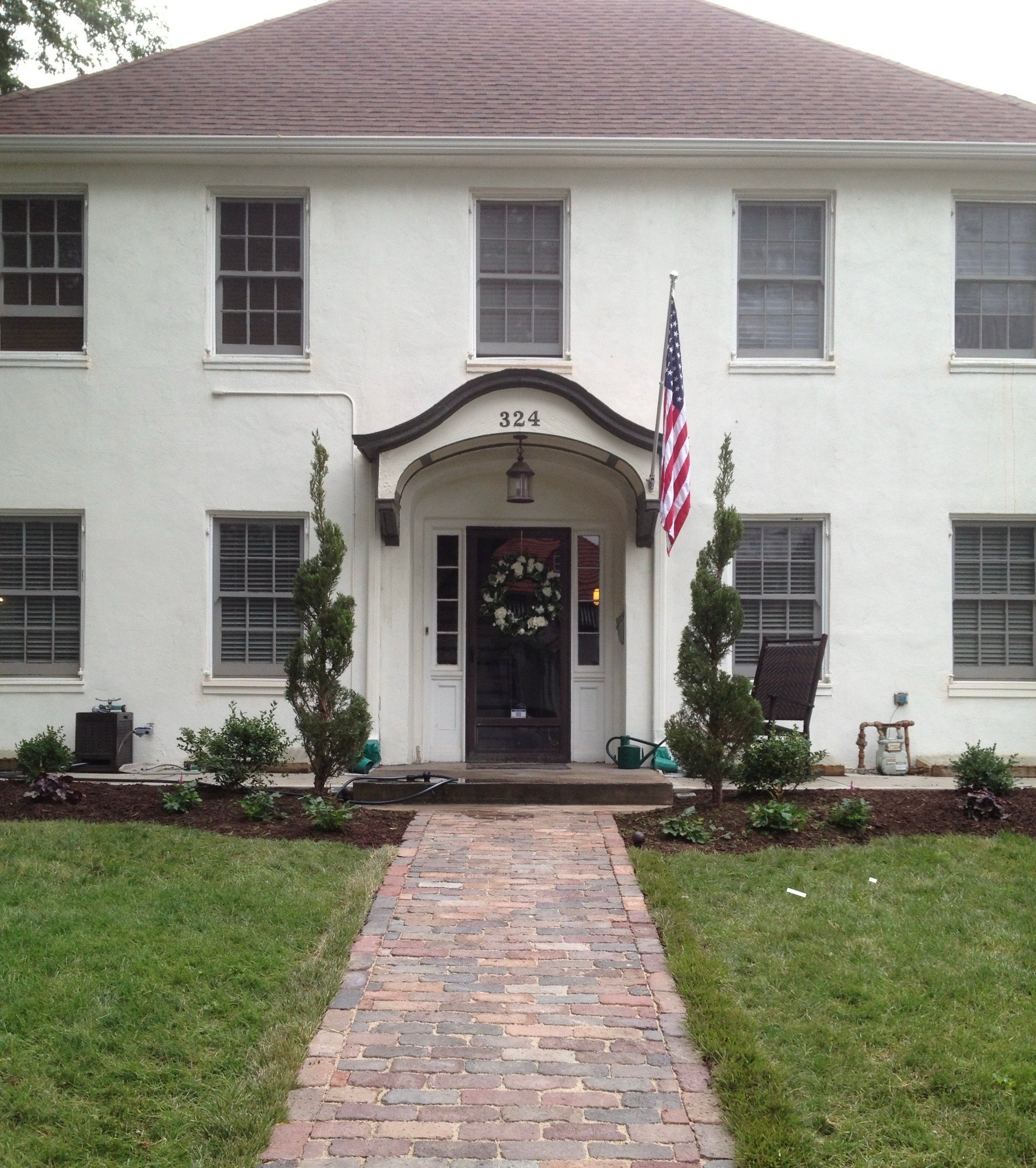 White colonial house with brick pathway leading to black front door, American flag, and wreath decoration