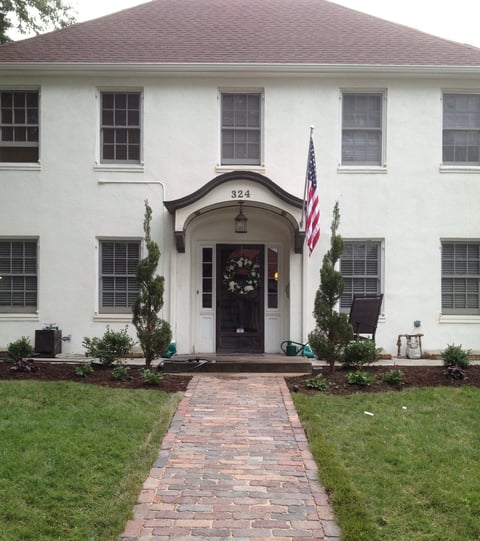 White colonial house with brick pathway leading to black front door, American flag, and wreath decoration