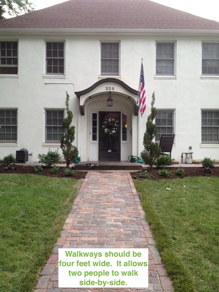 White two-story house with black door and American flag, brick walkway, green lawn, and design tip about walkway width overlaid at bottom