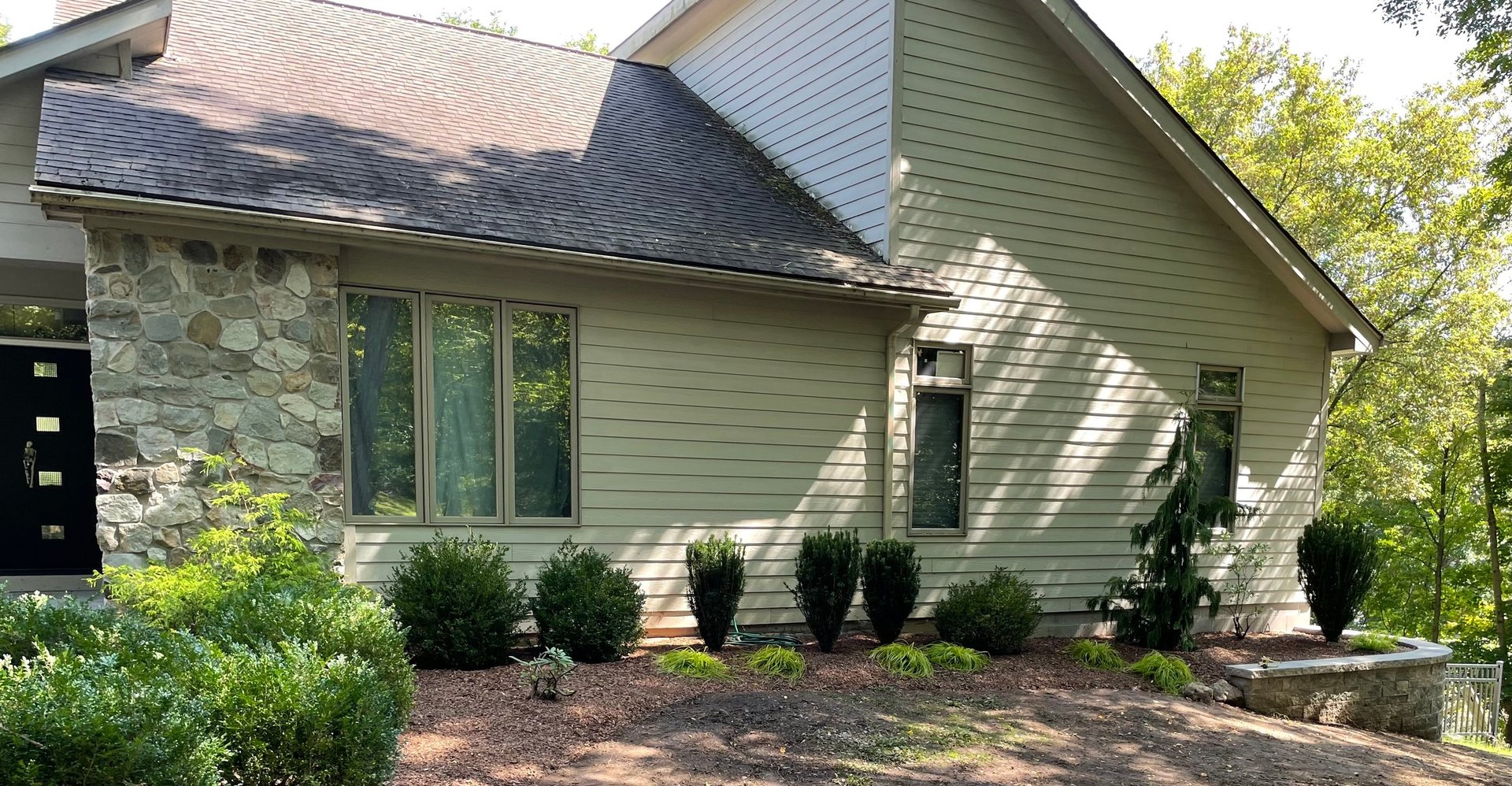 Modern residential house with stone and siding exterior, landscaped front with shrubs and mulch