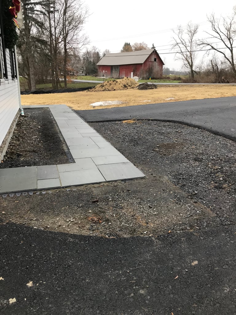 Driveway with stone pavers leading to a red barn on a rural farm property with bare trees