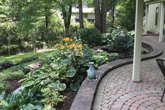 Garden with yellow flowers in ceramic pot, brick pathway, and trees in residential backyard