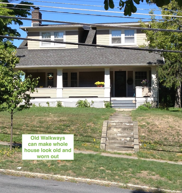 Two-story house with white trim and porch, green lawn, stone walkway, and sign reading Old Walkways can make whole house look old and worn out